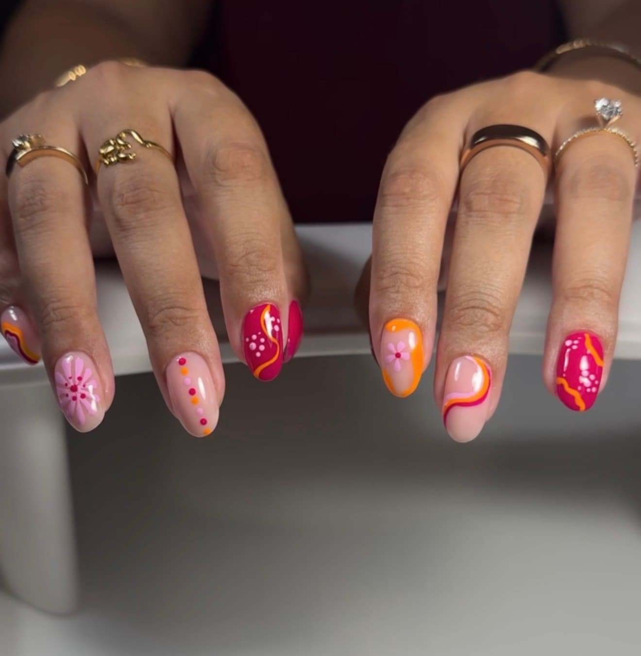 Both hands with short almond nails in pink, magenta and orange swirls, dots and daisies