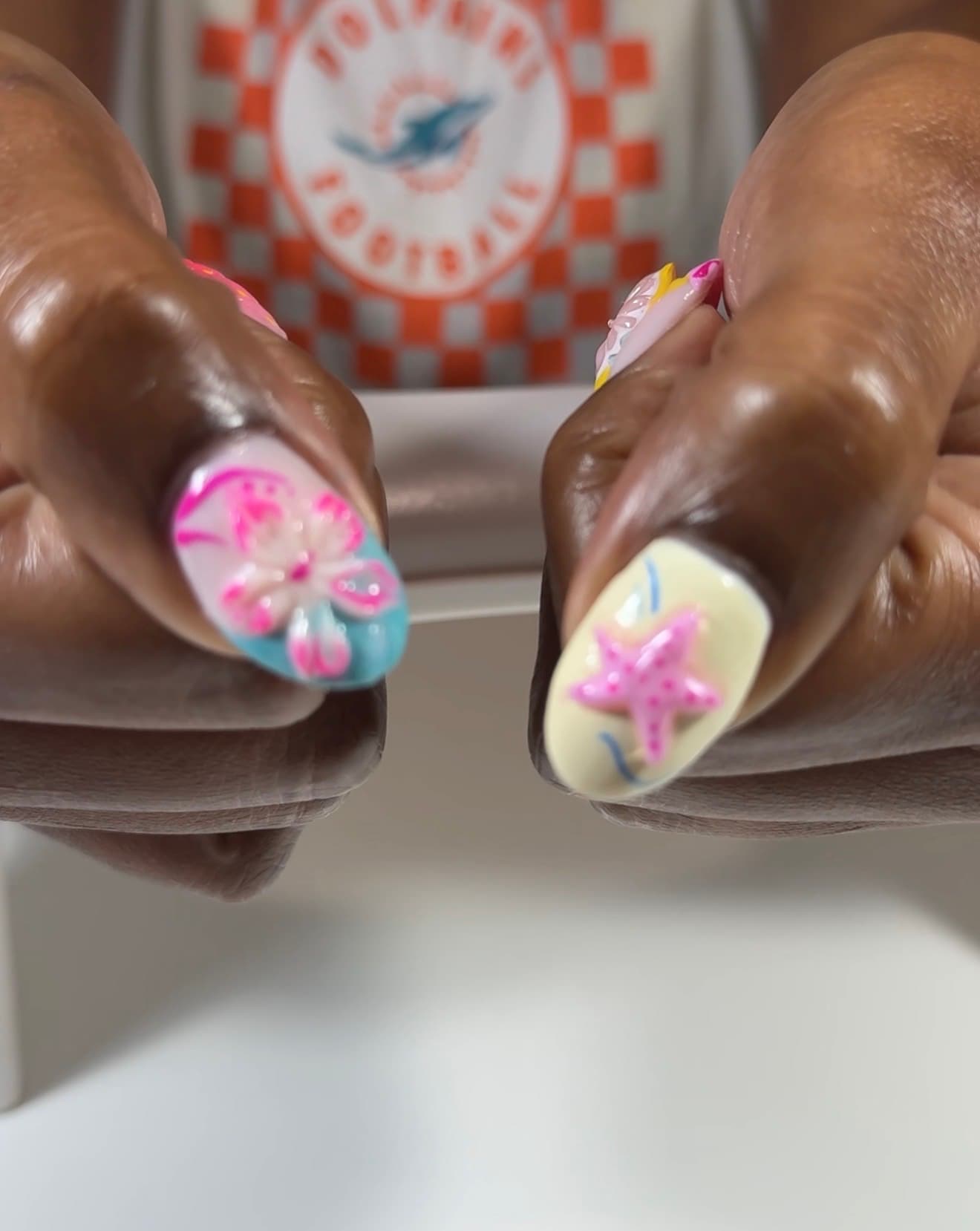 Close-up of two nails with sculpted 3D hibiscus and starfish art in pink, aqua and cream